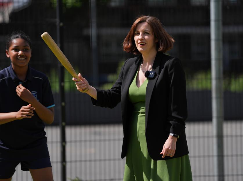 Bridget Phillipson holding a bat while a young girl smiles beside her.