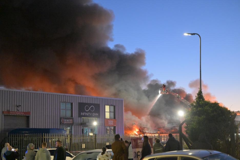 Firefighters fighting a large fire at Balloo Road industrial estate in Bangor, with thick smoke rising into the evening sky.