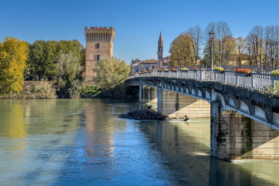 Bridge over the Adda River in Pizzighettone, with a medieval tower and church spire.