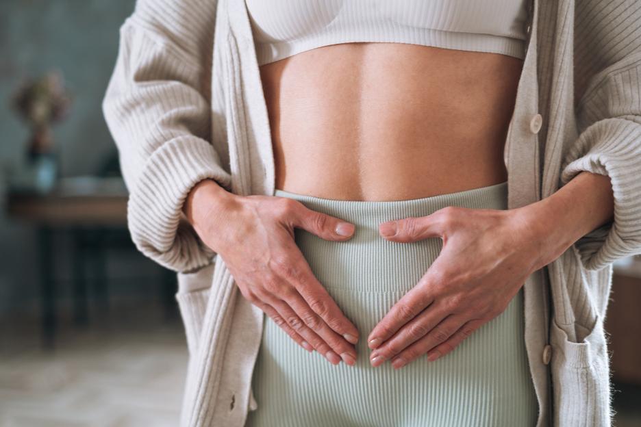 Woman Holding Lower Abdomen at Home, Portraying Self-Care During Menstrual Pain or Bloating Discomfort