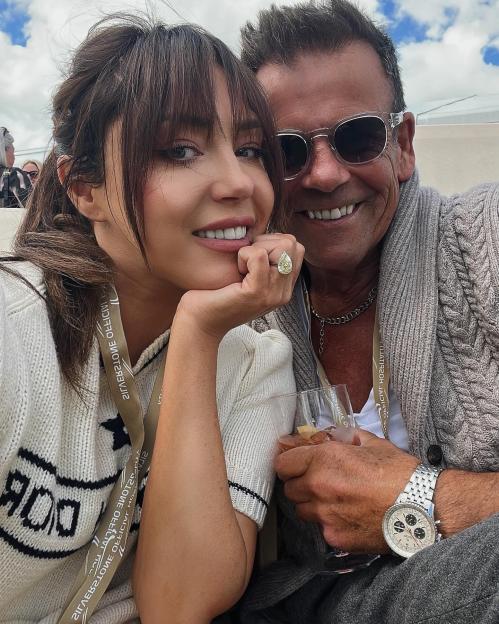 A woman with dark hair and a man in sunglasses smiling at the camera, with the man holding a drink.