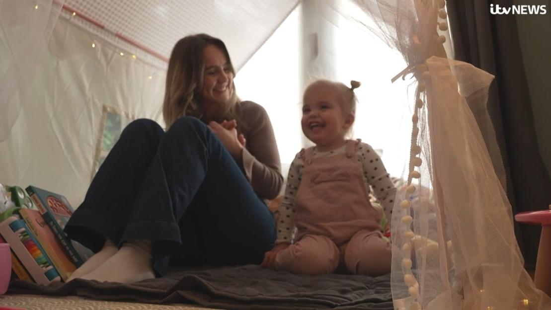 A woman and a young girl laugh together while sitting in a play tent.