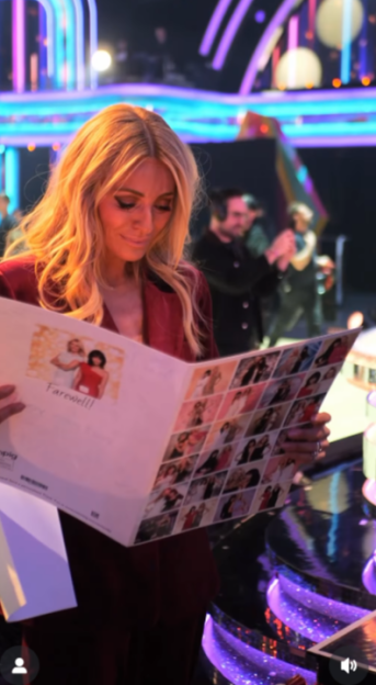 Woman in a red jacket holding a "Farewell!" card with pictures on it.