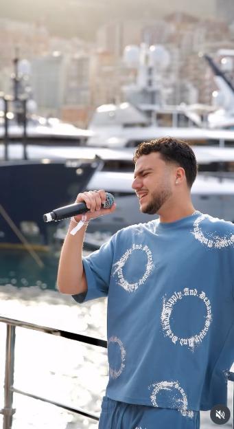 Junior Andre performing with a microphone in front of luxury yachts.