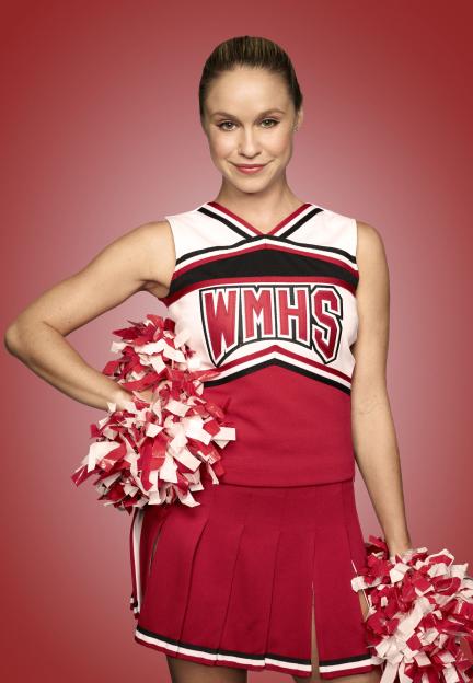 Becca Tobin as Kitty in a cheerleading uniform, holding pom-poms.