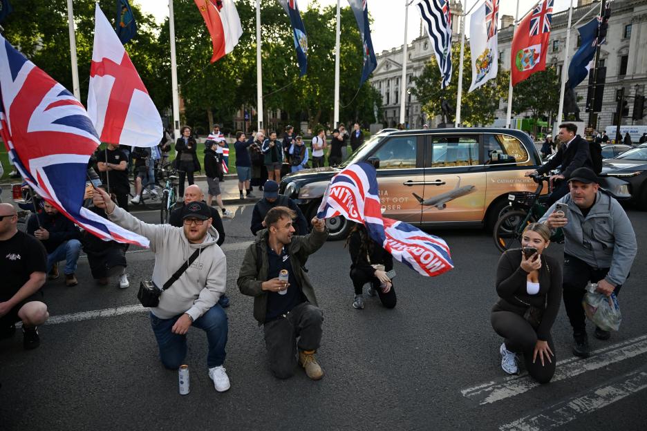 Protesters kneel in a street in London, holding Union Jack flags, following a knife attack in Belfast.