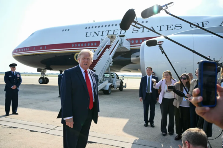 Donald Trump speaks in front of Air Force One as reporters hold microphones.