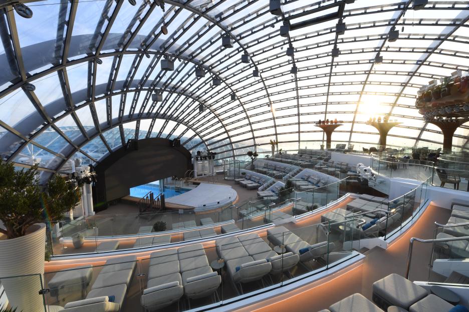 The interior of the Sun Princess cruise ship with a glass domed roof, an amphitheater-style seating area, and a pool.