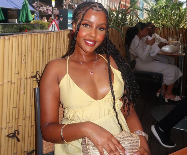 A woman in a yellow dress sitting at an outdoor restaurant, smiling.