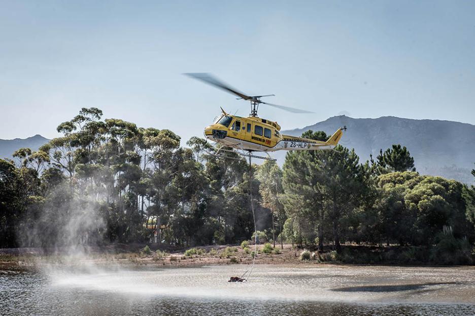 A Working On Fire Bell Huey chopper similar to the one that crashed above Hout Bay showing how its 1000 litre bucket scoops up water from rivers, dams, lakes or the sea to drop on wildfires in South Africa in areas where ground crews usually cannot a