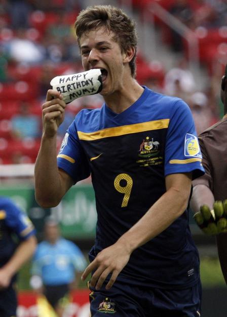 A young male soccer player in a blue and gold uniform holds a bandage with "HAPPY BIRTHDAY MUM" written on it.