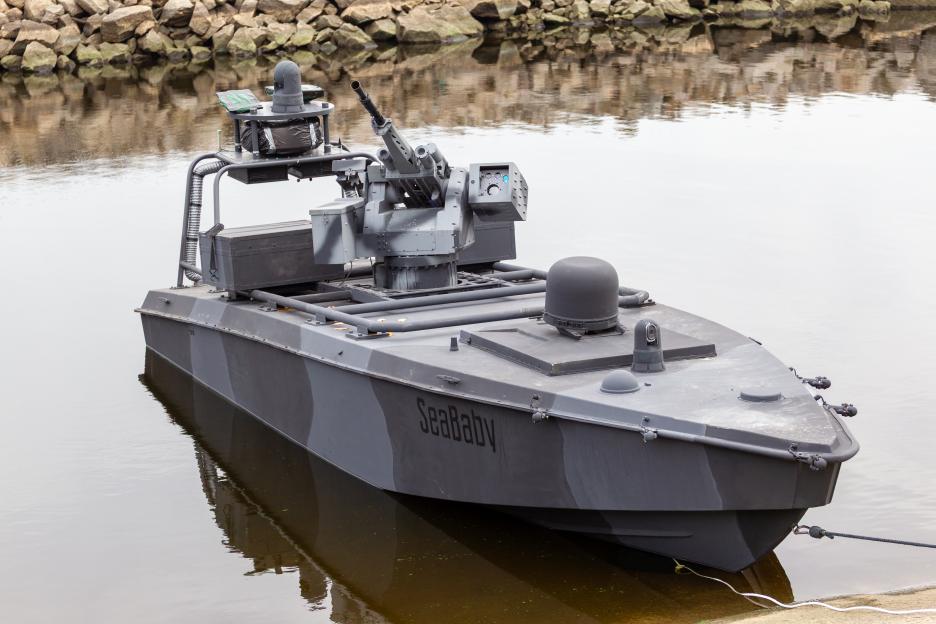 The Ukrainian Sea Baby unmanned surface vehicle, painted in gray and black camouflage, floats in the water with rocks in the background.