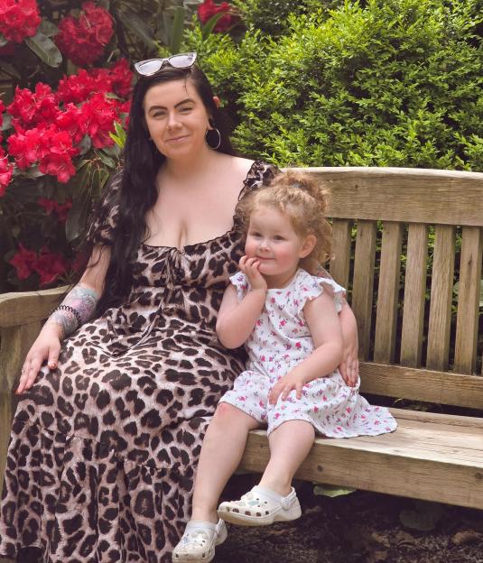 Courtney Sherwood and her daughter Penny Dunn sit on a bench with red flowers in the background.
