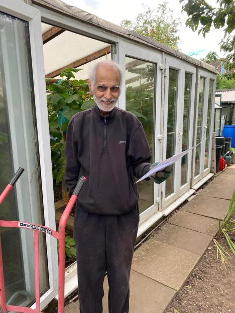 Bhim Kohli smiling and holding a piece of paper in front of a greenhouse.