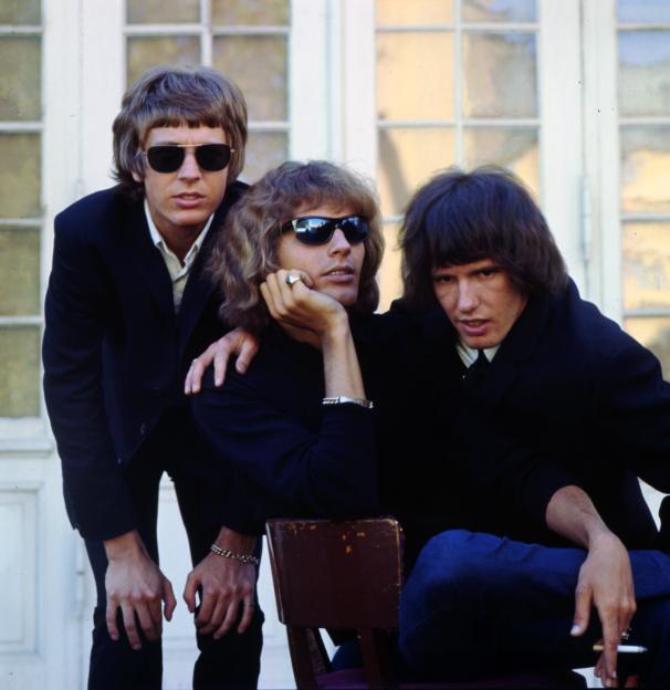 The Walker Brothers band members pose for a photo, one seated and two standing.