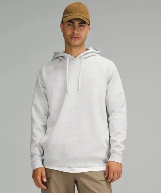 Man wearing a light gray pullover hoodie, a brown cap, and khaki pants.