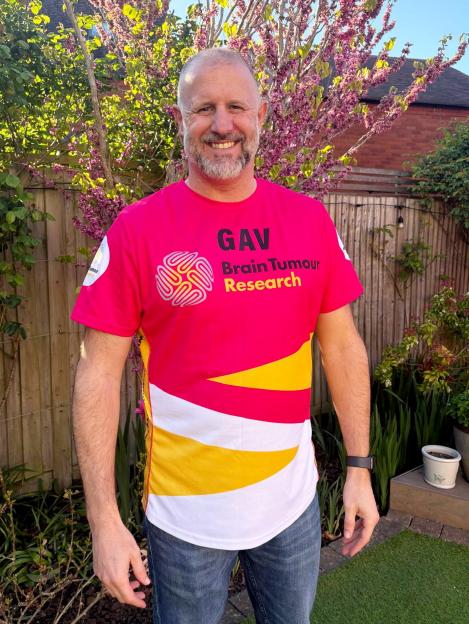 Man in a pink shirt that says "GAV Brain Tumour Research" with a yellow and white design at the bottom.