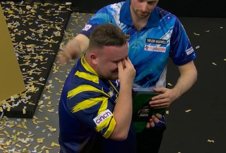 A darts player in a yellow and blue shirt cries while being comforted by another player.