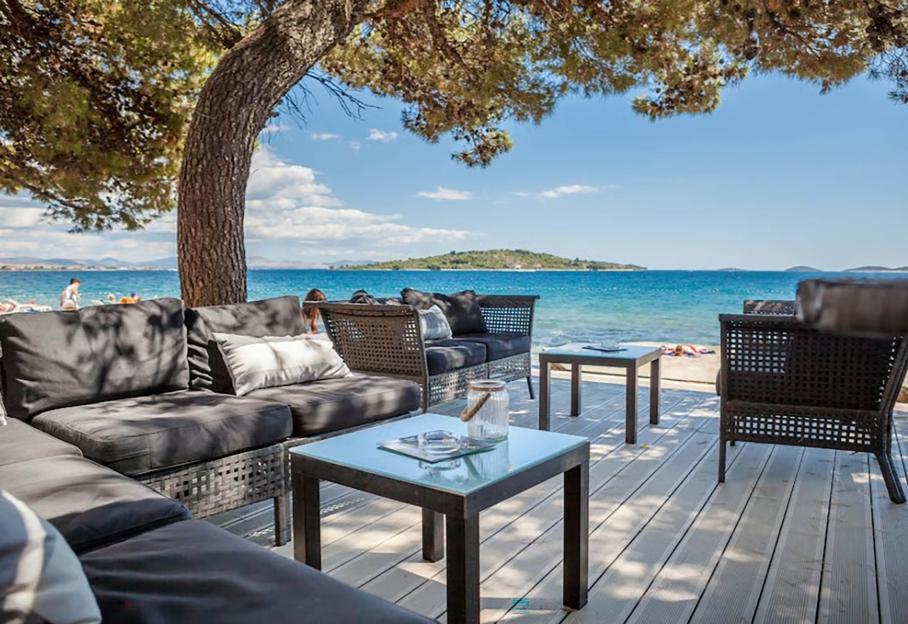 Outdoor lounge area with dark cushioned furniture on a deck overlooking a blue ocean.