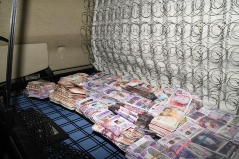 Bundles of cash filling a bed frame with an exposed spring mattress.