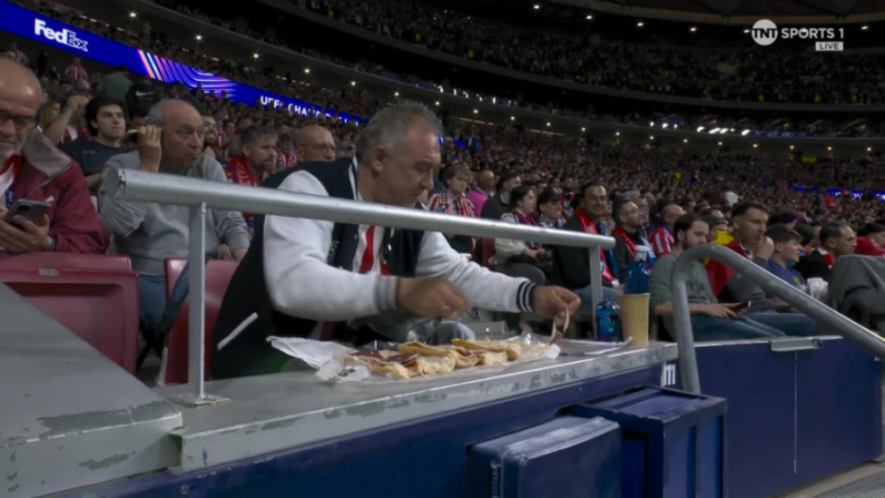 A man prepares sandwiches in the stands of a stadium during a sports game.