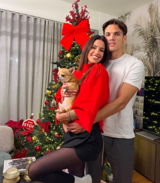 A man and a woman holding a chihuahua in front of a Christmas tree.