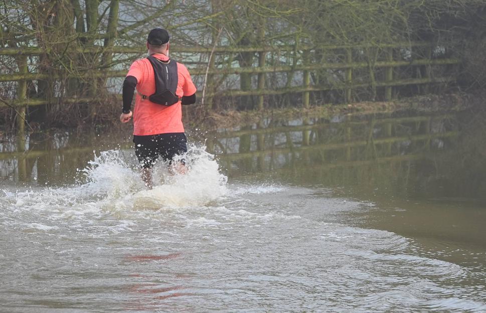 A man running through a flooded area, splashing water as he moves.