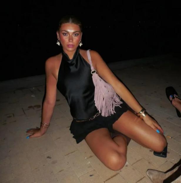 A woman in a black top and shorts sitting on the ground at night.