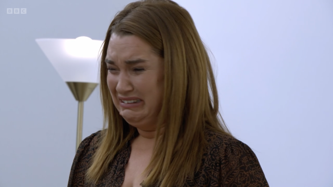 A woman with long brown hair looks distressed, with her mouth open and jaw clenched, wearing a patterned brown shirt.