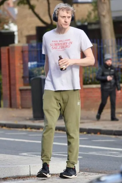 Comedian James Acaster leaves a gym session in London, holding a drink and wearing headphones.