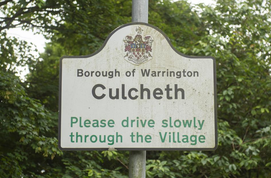 A sign for the Borough of Warrington, Culcheth, with the text "Please drive slowly through the Village".