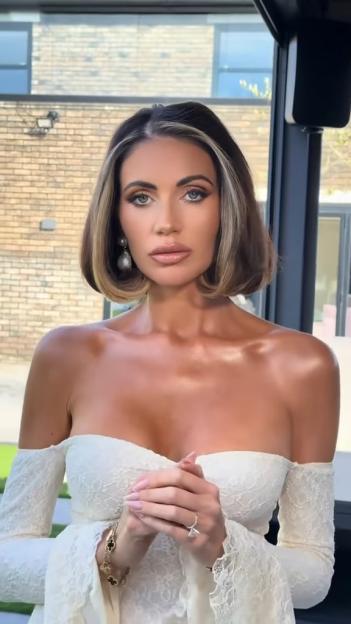 Amy Childs wearing a white lace off-the-shoulder wedding dress with long sleeves and a large diamond ring on her finger.