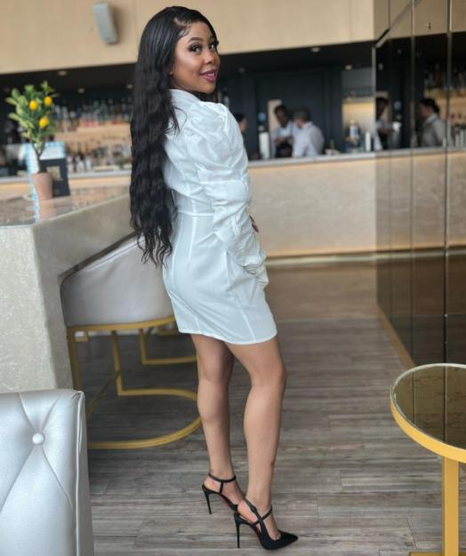 Hadiza Atunse posing in a white dress and black high heels, looking over her shoulder with a smile.