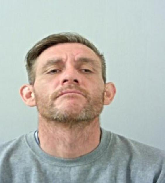 Mugshot of a man with short brown hair, beard, and mustache, wearing a gray sweatshirt.