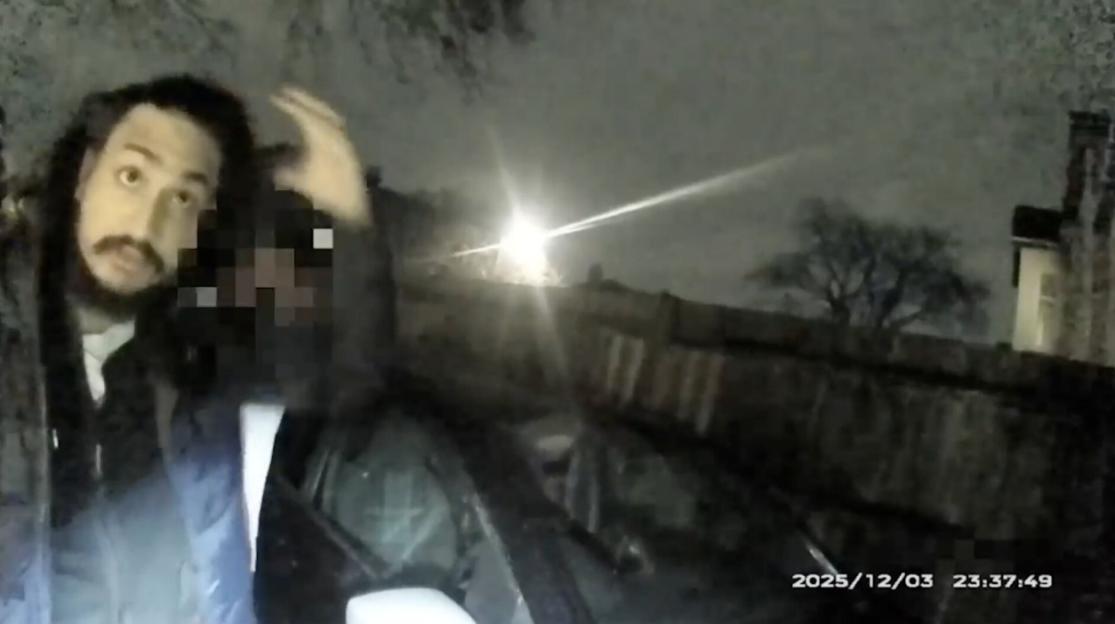 Footage showing a man with long hair and a beard looking at a camera, with another person's face pixelated, taken at night.