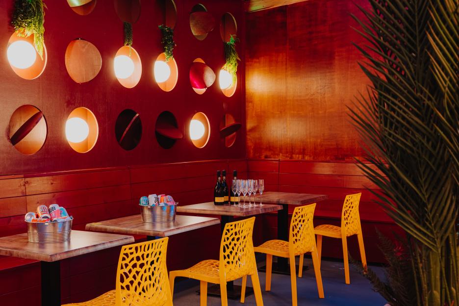 Indoor seating area with red walls, circular light fixtures, yellow chairs, and tables with drinks.