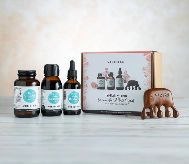 The Viridian Tri-Hair System, featuring "Hair Support Complex" capsules, "Organic Hair Growth Liquid," "Organic Hair Restore Serum," and a wooden scalp massager, packaged together.