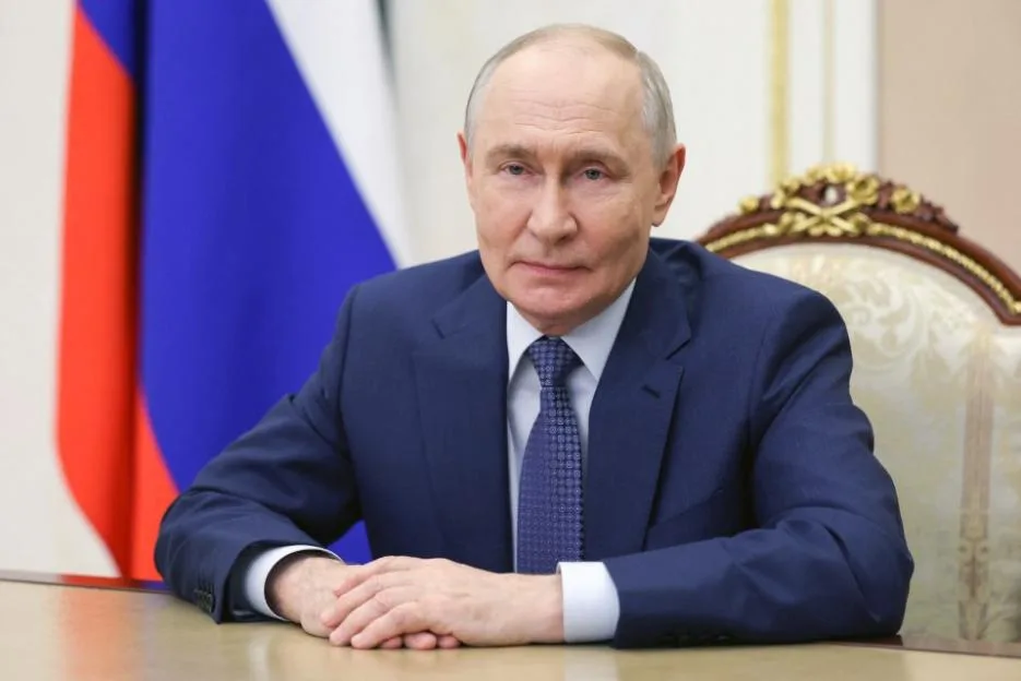 Russian President Vladimir Putin seated at a desk in front of a Russian flag.