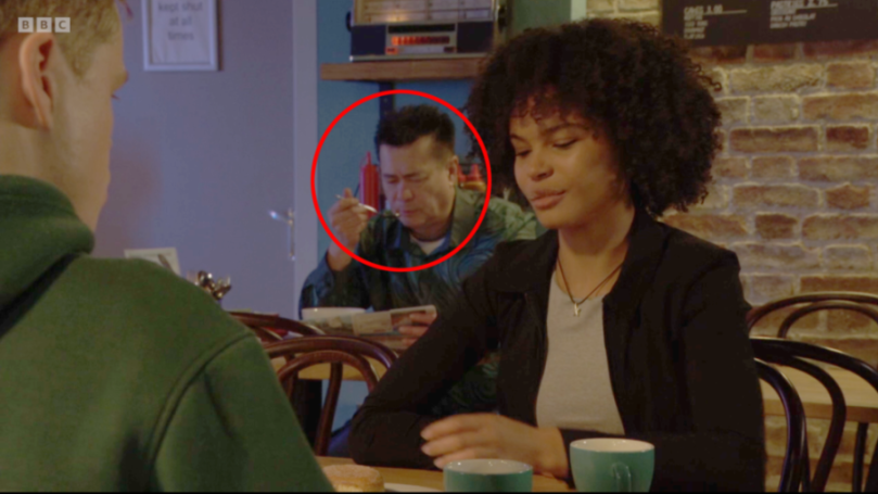 A man eating nothing in the background of a cafe scene, circled in red.