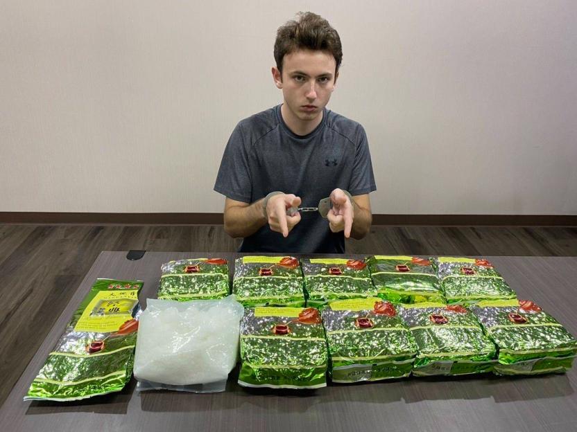 A man in handcuffs seated at a table with crystal meth and bags of tea, possibly concealing more drugs.