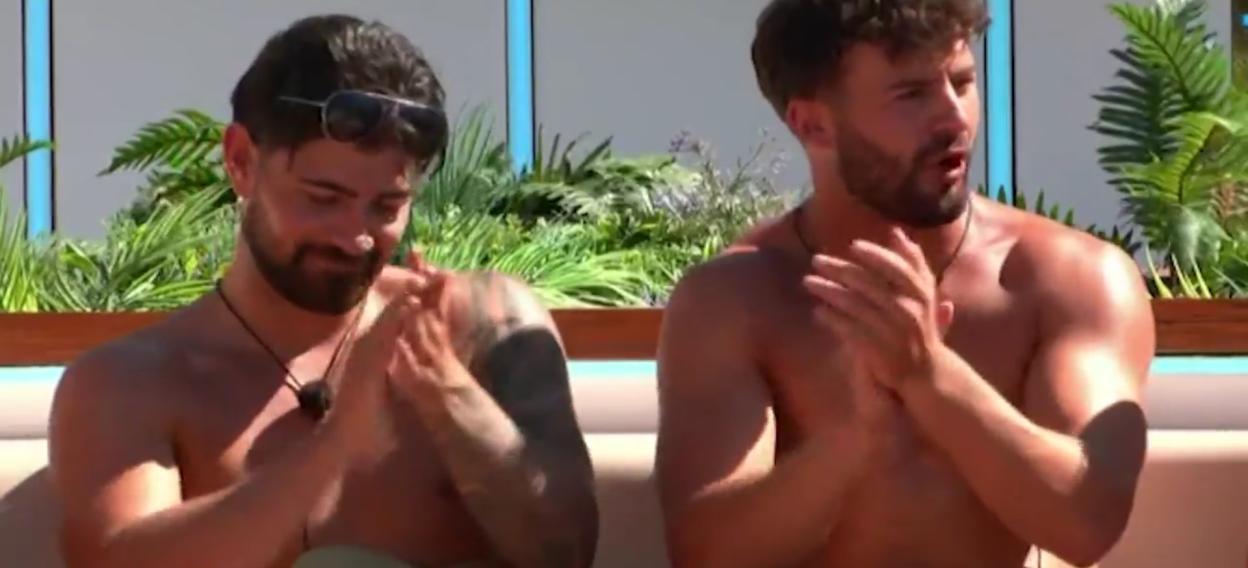 Two shirtless men clap their hands, one with sunglasses pushed onto his head.