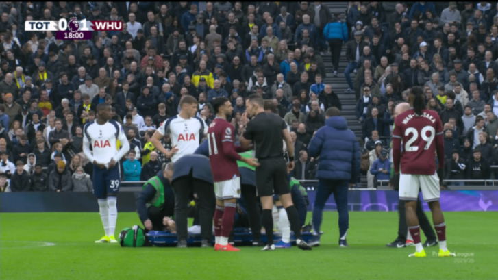 Soccer players and staff surround an injured player being attended to by medics on the field during a Tottenham Hotspur vs. West Ham United match.