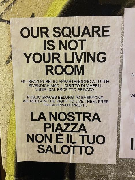 A protest poster in Palermo, Italy, reading "OUR SQUARE IS NOT YOUR LIVING ROOM" in English and Italian, highlighting public space ownership.