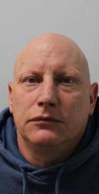 Mugshot of a bald man in a blue hoodie looking forward.