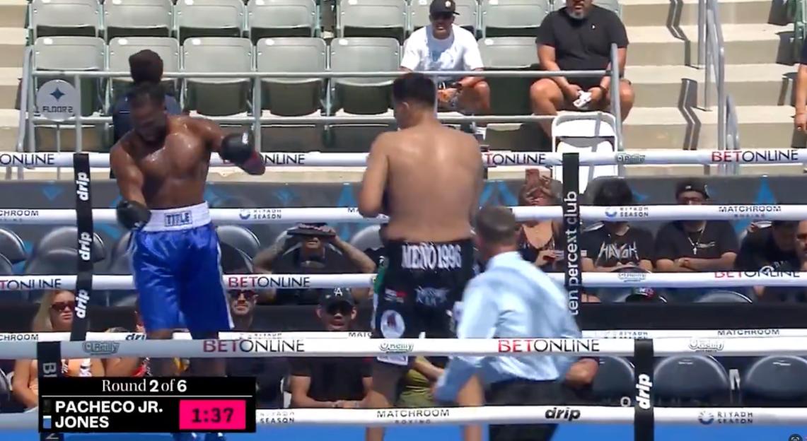 Two shirtless male boxers in a ring with a referee.