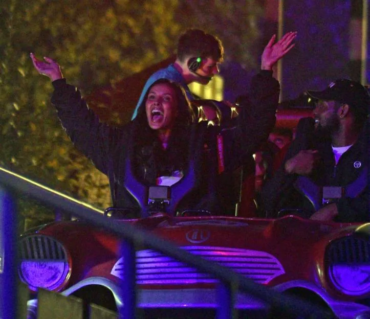 Maya Jama riding a roller coaster at Thorpe Park with her arms raised and shouting in excitement.
