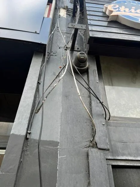 A CCTV camera and tangled wires on a neglected building facade along Uxbridge Road in London.