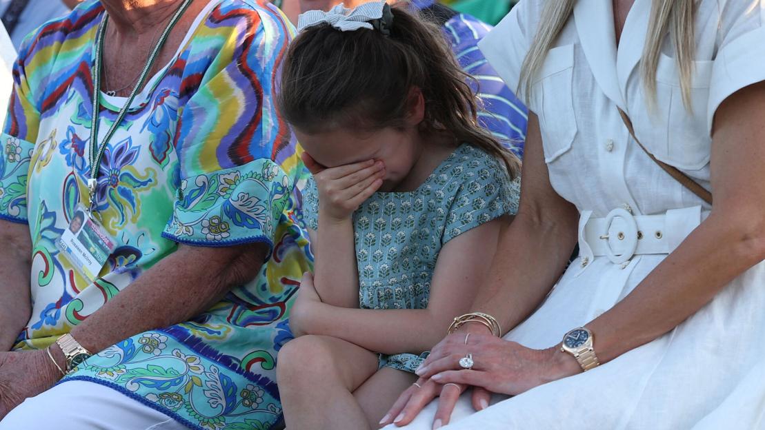 A young girl cries with her face in her hands, seated between two women.