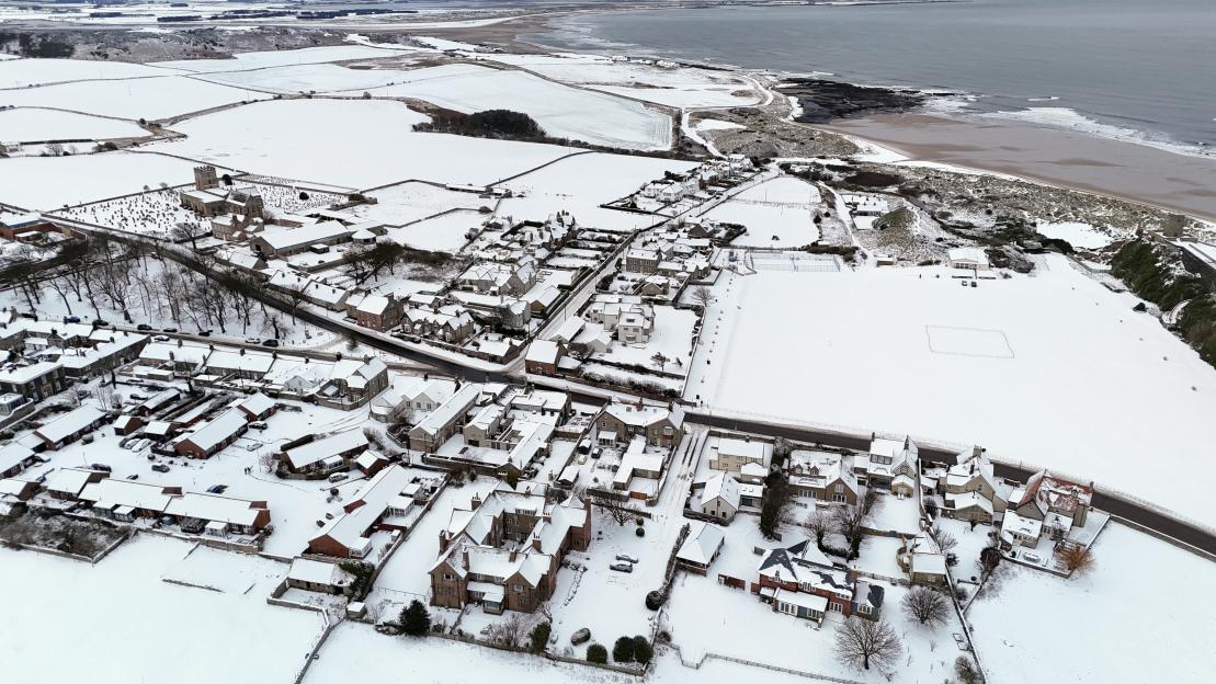 Aerial view of Bamburgh, Northumberland, covered in snow with the coast visible.