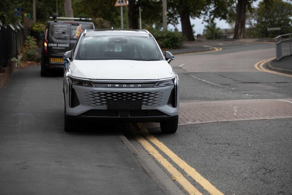 A white and gray Omoda car parked on double yellow lines with a van behind it.